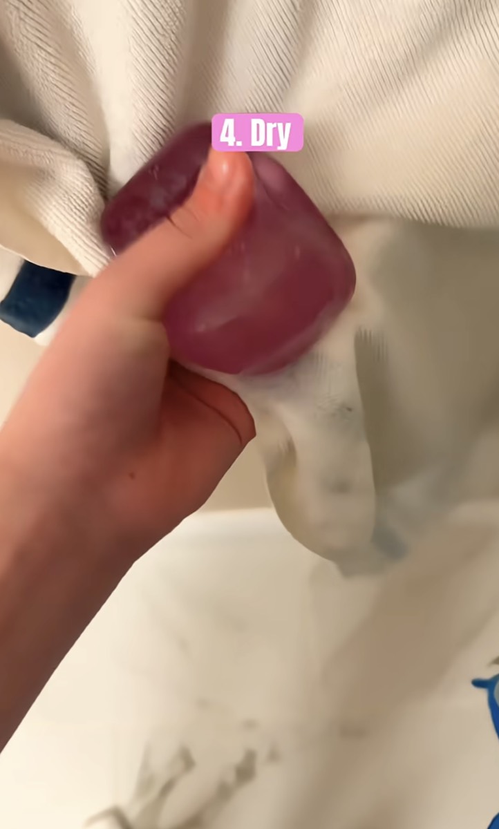 A purple NeeDoh cube being blotted dry in a white towel