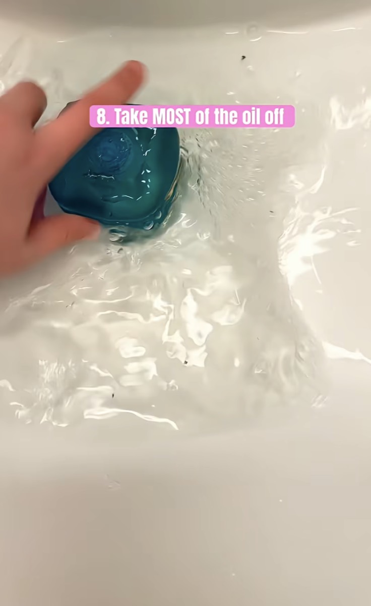 A teal NeeDoh cube held under running water to rinse most of the oil away