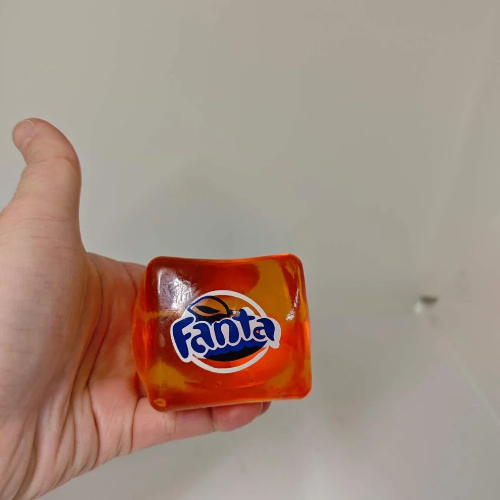 Translucent orange gel cube with a Fanta sticker held in a hand