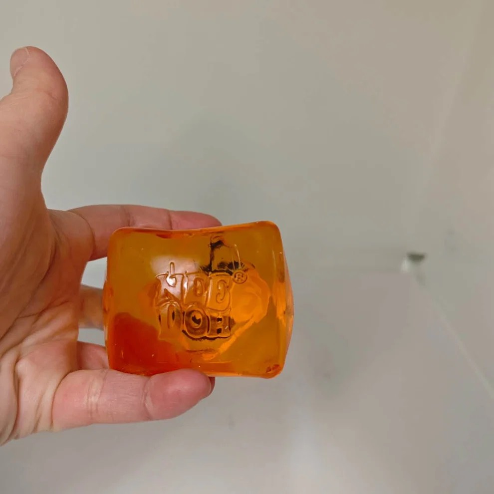 Orange squishy cube showing raised NeeDoh lettering in the gel