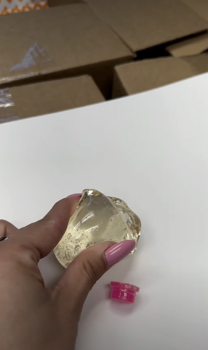 Amber blob of NeeDoh filling held in one hand beside the collapsed pink shell it came from