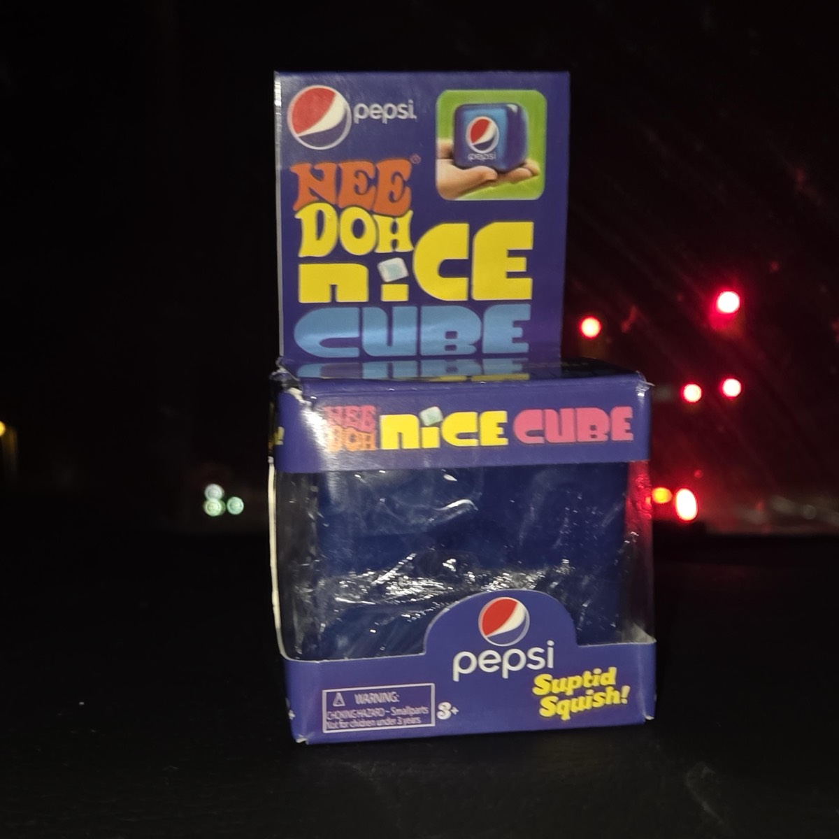 Purple Pepsi carton holding the navy squishy cube, photographed at night in a car