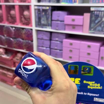 Fist squeezing the navy Pepsi squishy cube in front of a toy store shelf